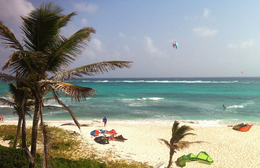 Plaža na Barbadosu z barvito kitesurfing opremo, palmami in turkiznim morjem – priljubljena destinacija za vodne športe
