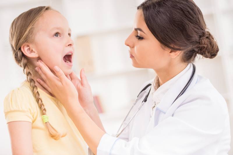 Otorinolaringolog pregleduje grlo otroka zaradi suma na povečano žrelnico.
