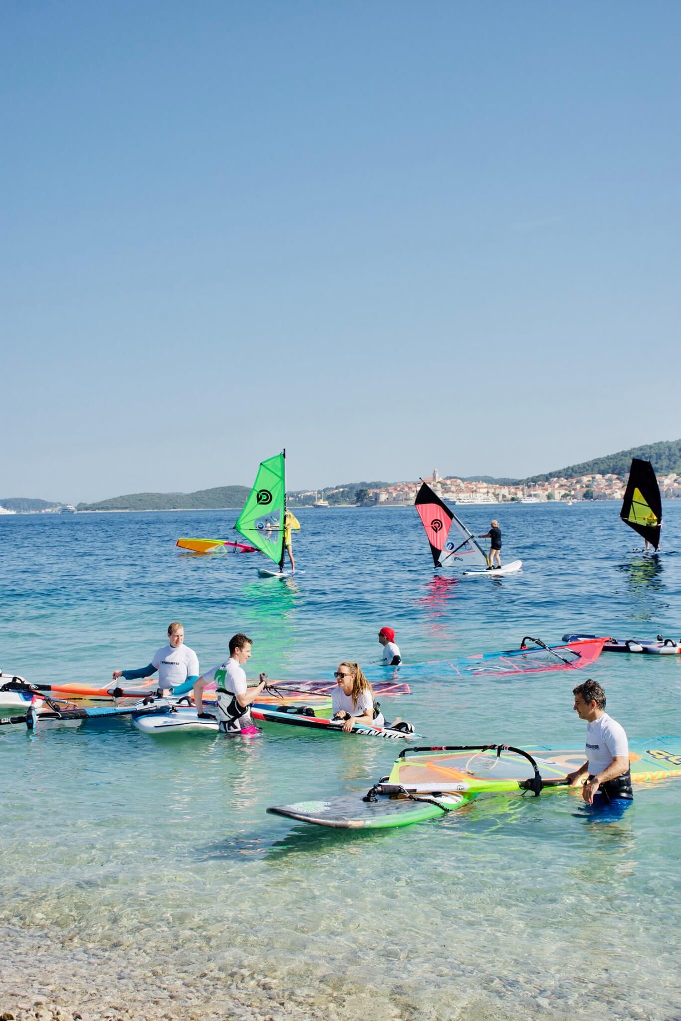 Windsurferji z opremo, deksami in jadri ob vhodu v mirno morje na Pelješcu