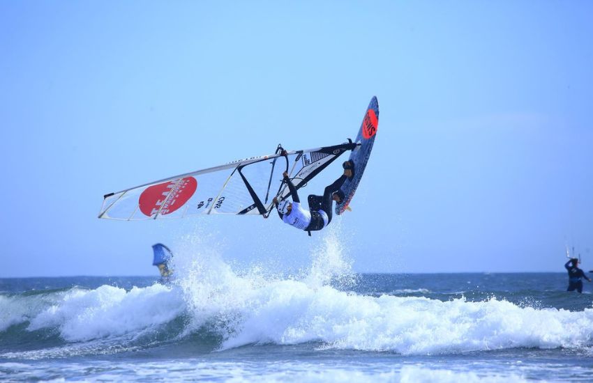 Windsurfer med zračnim manevrom nad valovi, z nagnjeno desko in jadrom
