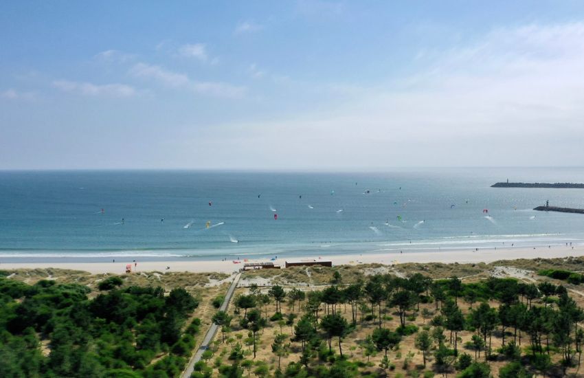 Panoramski pogled na belo peščeno plažo in številnimi jadralci ali kite surferji s pisanimi jadri v morju