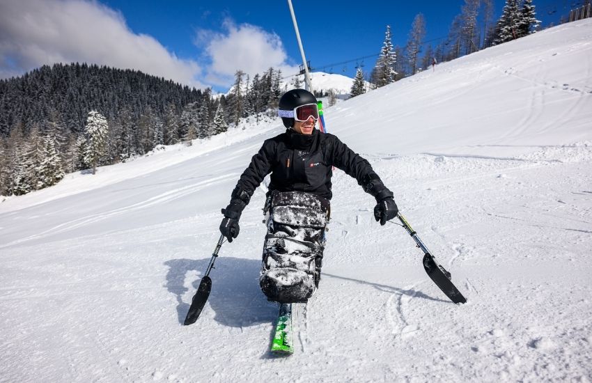 Na sliki je para&scaron;portnik Anej Doplihar, ki se uči smučanja na monoskiju, kar je prilagojena oprema za invalide. Nahaja se na zasneženem smuči&scaron;ču, oblečena v temno smučarsko opremo in nosi čelado. Za ravnotežje in usmerjanje uporablja dve kratki palici z majhnimi smučkami na koncu.